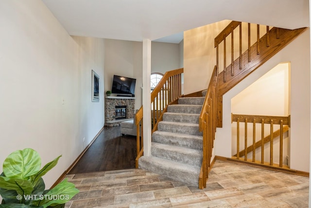 stairway featuring baseboards, a fireplace, and wood finished floors
