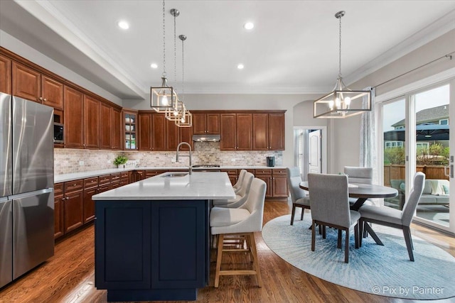 kitchen featuring crown molding, light countertops, freestanding refrigerator, a chandelier, and under cabinet range hood