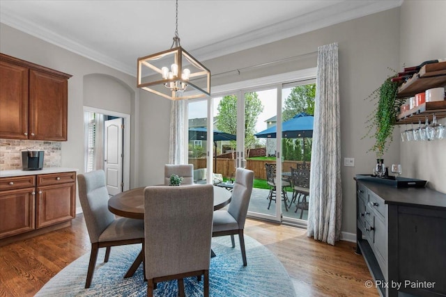dining space with light wood-type flooring, ornamental molding, and a notable chandelier