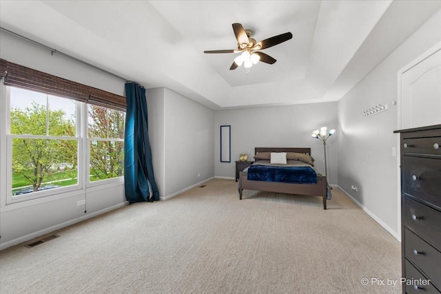 carpeted bedroom with visible vents, a ceiling fan, baseboards, and a tray ceiling