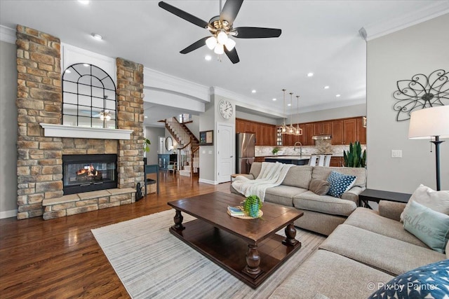 living room with a multi sided fireplace, a ceiling fan, baseboards, ornamental molding, and stairway