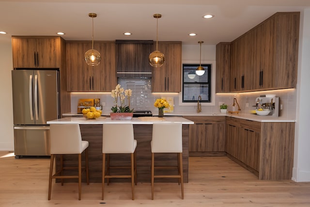 kitchen with freestanding refrigerator, light wood-type flooring, light countertops, a sink, and backsplash