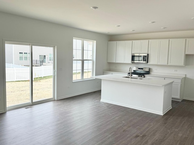 kitchen with appliances with stainless steel finishes, dark wood-style flooring, a kitchen island with sink, and light countertops
