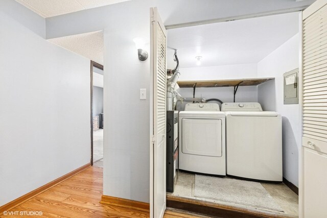 washroom with electric panel, laundry area, washing machine and clothes dryer, baseboards, and light wood-style floors