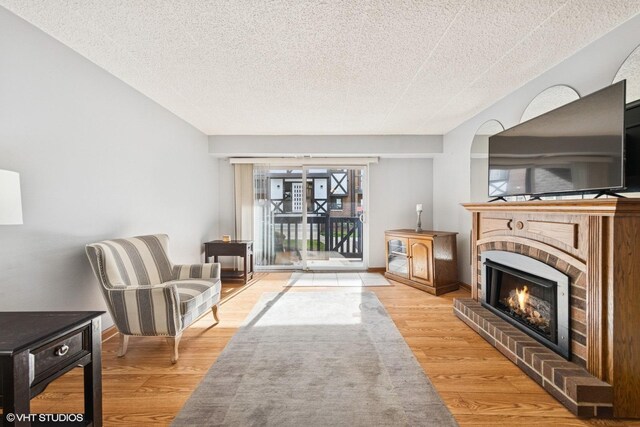 living area with baseboards, a textured ceiling, light wood-style flooring, and a fireplace