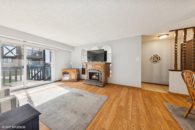 living room featuring baseboards, a textured ceiling, wood finished floors, and a fireplace