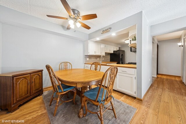 dining area featuring a textured ceiling, ceiling fan, baseboards, and light wood-style floors