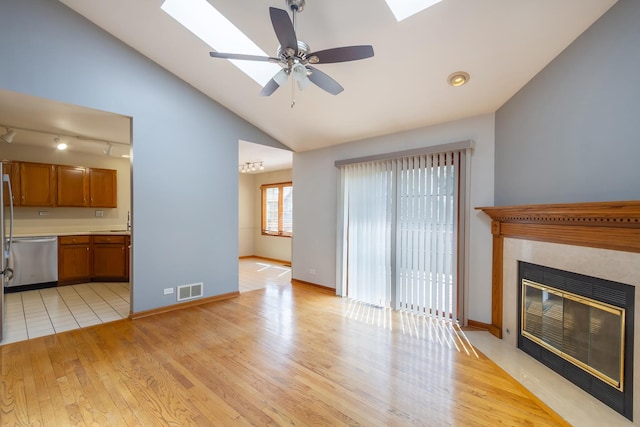 unfurnished living room with vaulted ceiling with skylight, ceiling fan, visible vents, a fireplace with flush hearth, and light wood-style floors