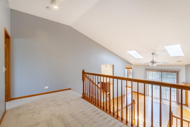 hallway featuring baseboards, carpet flooring, vaulted ceiling with skylight, and an upstairs landing