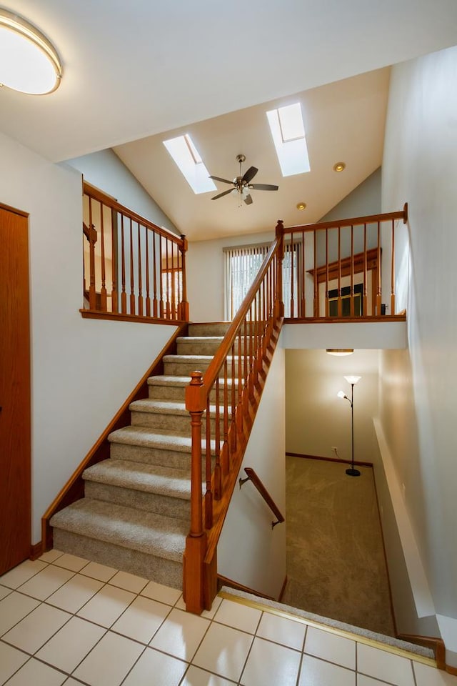 stairway featuring baseboards, tile patterned flooring, and vaulted ceiling with skylight