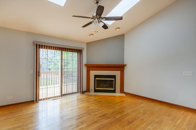 unfurnished living room with light wood-style flooring, a ceiling fan, baseboards, a fireplace with flush hearth, and lofted ceiling with skylight