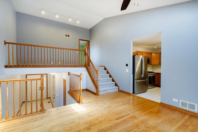 stairs with a ceiling fan, visible vents, vaulted ceiling, rail lighting, and wood finished floors