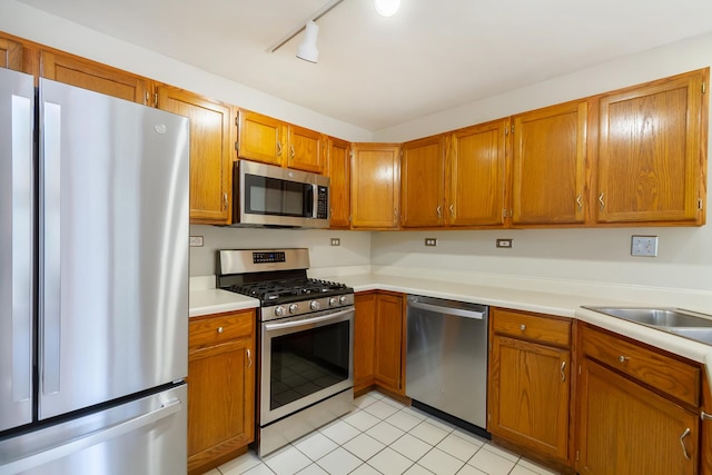 kitchen with light tile patterned flooring, light countertops, brown cabinets, a sink, and appliances with stainless steel finishes