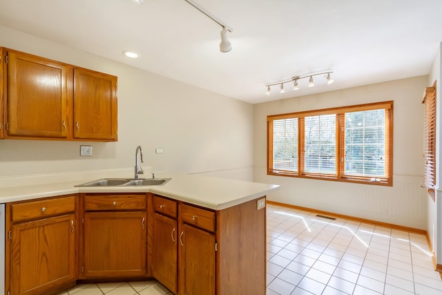 kitchen with brown cabinetry, a sink, a peninsula, and light countertops