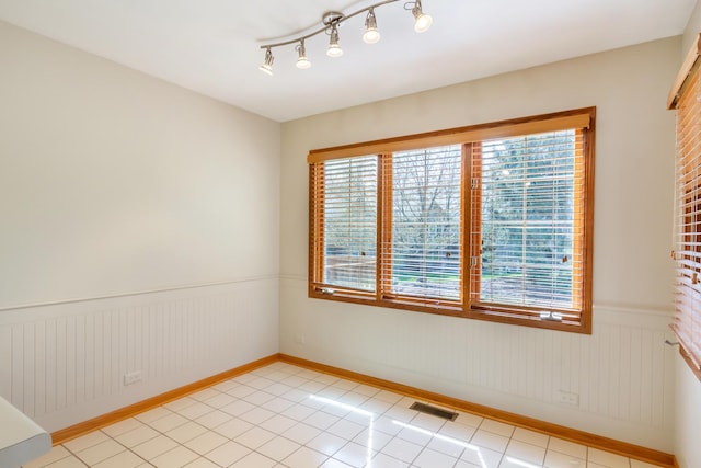 spare room with light tile patterned flooring, visible vents, a healthy amount of sunlight, and a wainscoted wall