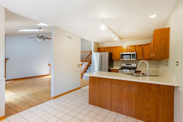 kitchen with a sink, brown cabinetry, stainless steel appliances, a peninsula, and visible vents