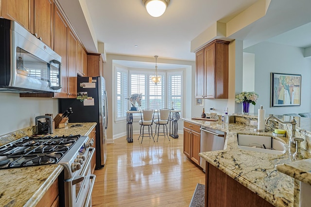 kitchen with light stone countertops, a sink, light wood-style floors, brown cabinetry, and appliances with stainless steel finishes