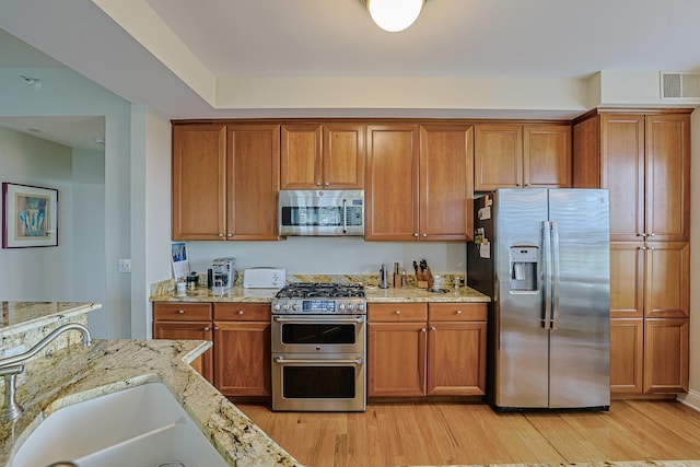kitchen featuring visible vents, stainless steel appliances, light wood-type flooring, and brown cabinets