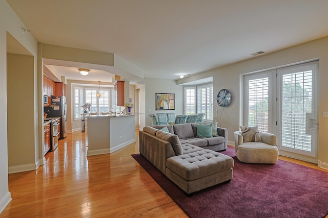 living room featuring visible vents, baseboards, a wealth of natural light, and light wood-style floors