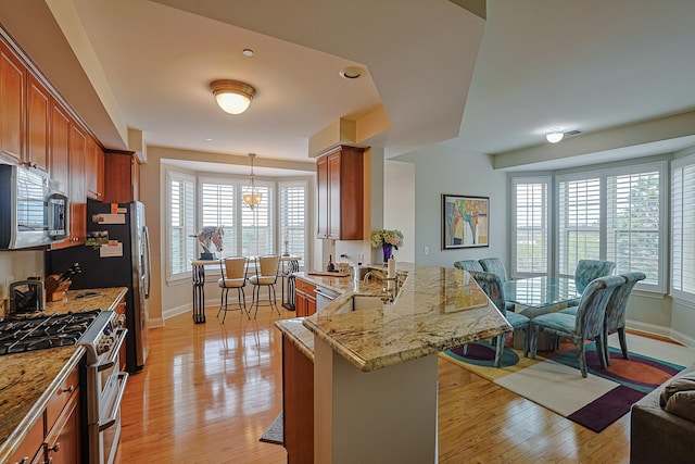 kitchen with open floor plan, brown cabinets, stainless steel appliances, and light wood-style floors