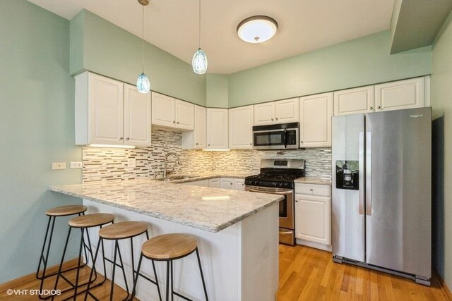 kitchen featuring pendant lighting, a sink, white cabinets, a peninsula, and stainless steel appliances