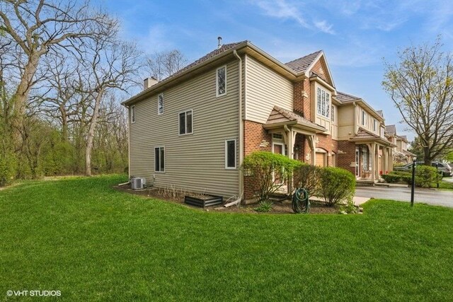 view of property exterior featuring brick siding, central AC, a yard, and a chimney
