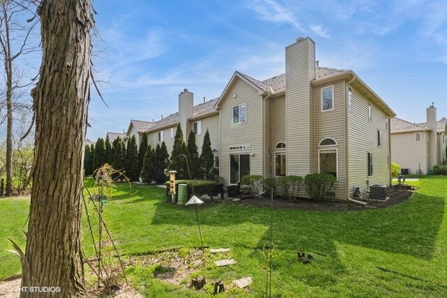 back of property with a chimney, a yard, and central AC