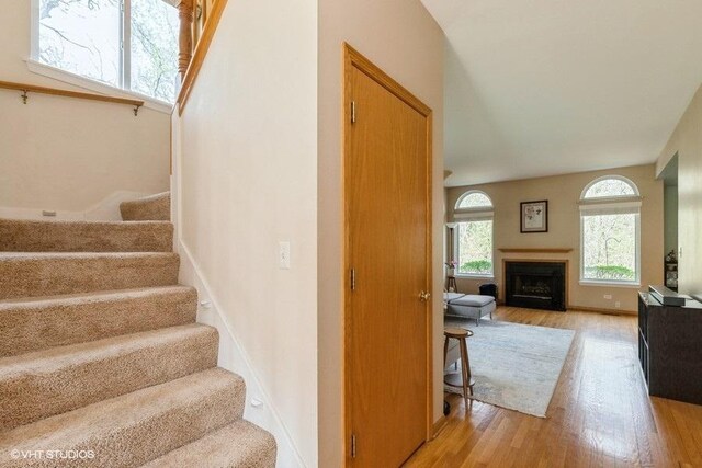 staircase featuring baseboards, a fireplace, and wood finished floors