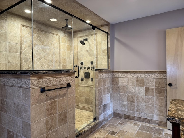 bathroom featuring wainscoting, recessed lighting, tile walls, stone tile flooring, and a stall shower