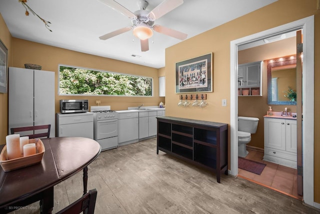 kitchen featuring a ceiling fan, white gas stove, stainless steel microwave, a sink, and light wood-style flooring