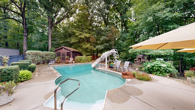view of swimming pool featuring fence, a water slide, a fenced in pool, an outbuilding, and a patio area