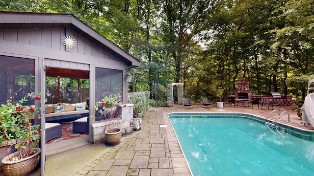 pool featuring a patio and an outdoor living space with a fireplace