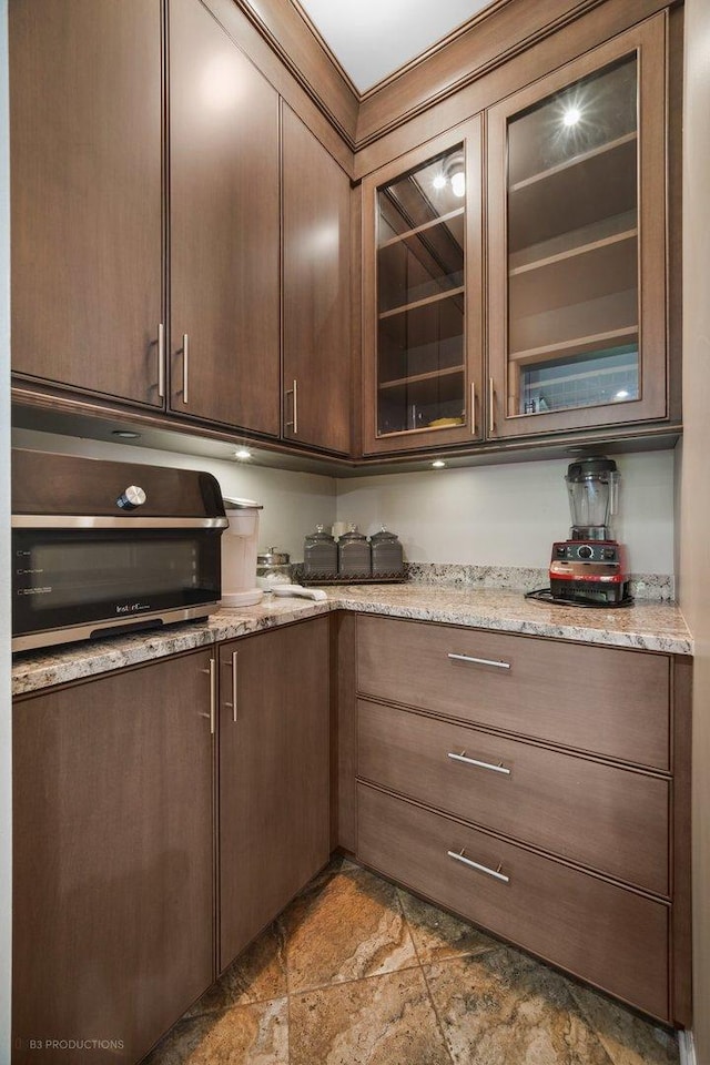 kitchen featuring glass insert cabinets, stone finish floor, and light stone counters
