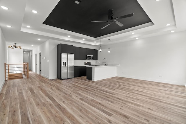 kitchen with appliances with stainless steel finishes, dark cabinetry, a tray ceiling, and open floor plan