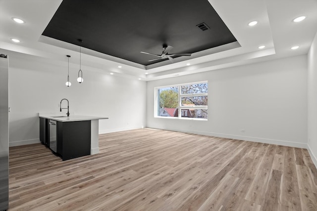 unfurnished living room featuring visible vents, a sink, a raised ceiling, and light wood finished floors