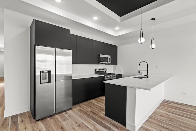 kitchen featuring appliances with stainless steel finishes, a sink, baseboards, a peninsula, and dark cabinetry