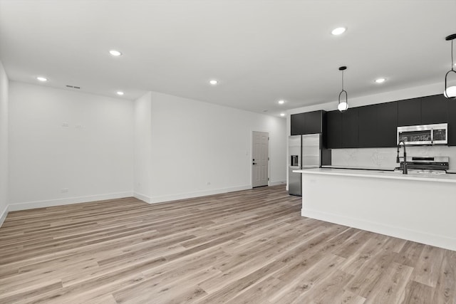 kitchen featuring recessed lighting, light countertops, dark cabinetry, light wood-style flooring, and stainless steel appliances