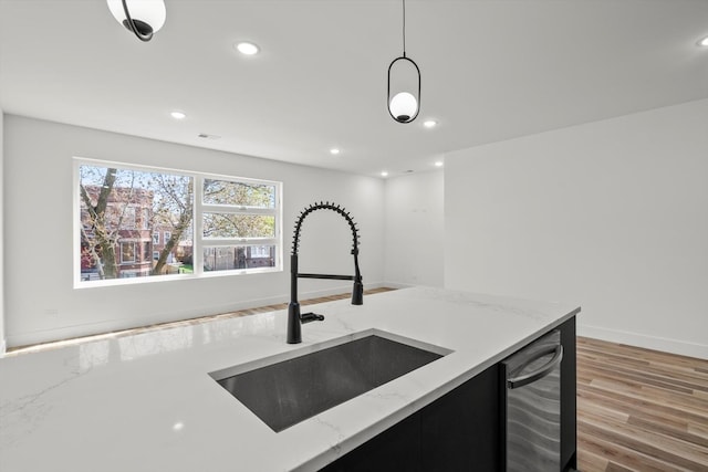 kitchen with hanging light fixtures, dishwasher, a sink, light stone counters, and light wood finished floors