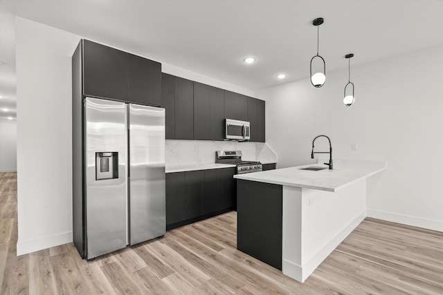 kitchen featuring appliances with stainless steel finishes, a sink, a peninsula, light wood-style floors, and dark cabinetry