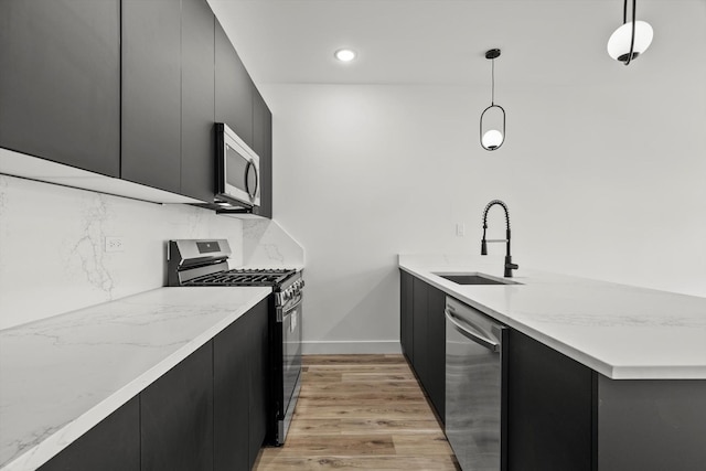 kitchen featuring a sink, light wood finished floors, dark cabinetry, stainless steel appliances, and a peninsula