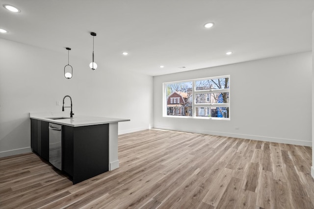 kitchen featuring stainless steel dishwasher, light wood-style floors, open floor plan, dark cabinetry, and a sink