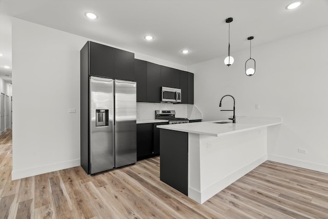 kitchen with appliances with stainless steel finishes, a sink, dark cabinetry, light countertops, and a peninsula