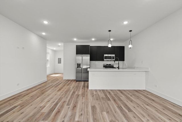 kitchen with appliances with stainless steel finishes, light countertops, light wood finished floors, dark cabinets, and recessed lighting