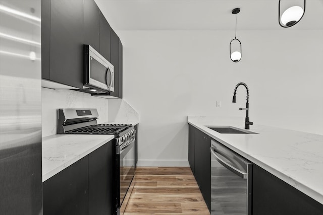 kitchen featuring a sink, hanging light fixtures, dark cabinetry, and stainless steel appliances