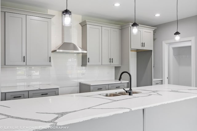 kitchen with wall chimney exhaust hood, light stone countertops, a sink, and decorative backsplash