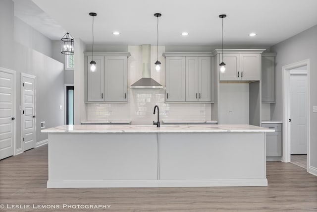 kitchen featuring backsplash, a center island with sink, gray cabinets, and wall chimney exhaust hood