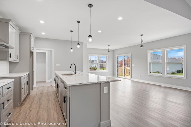 kitchen with light wood-type flooring, a center island with sink, baseboards, and a sink