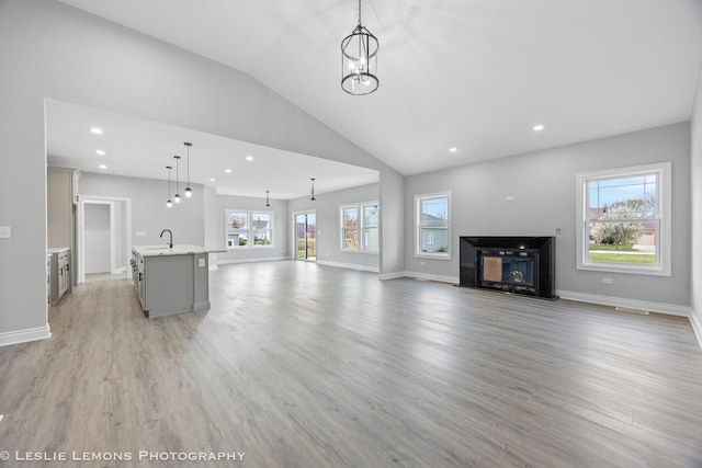 unfurnished living room featuring light wood-style floors, a fireplace with flush hearth, lofted ceiling, and a sink