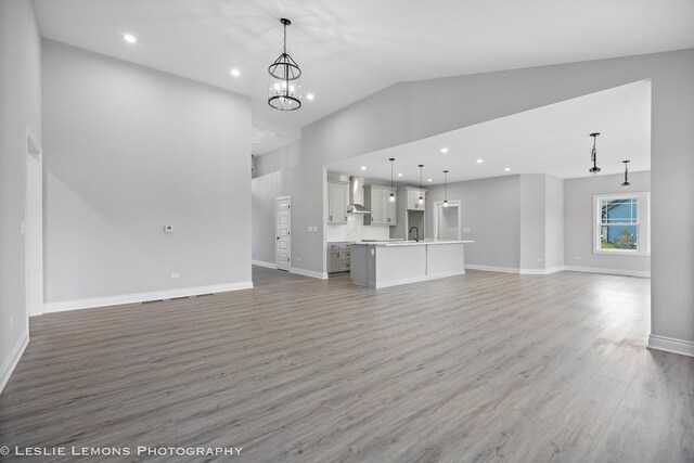 unfurnished living room featuring a sink, light wood-style flooring, high vaulted ceiling, and baseboards