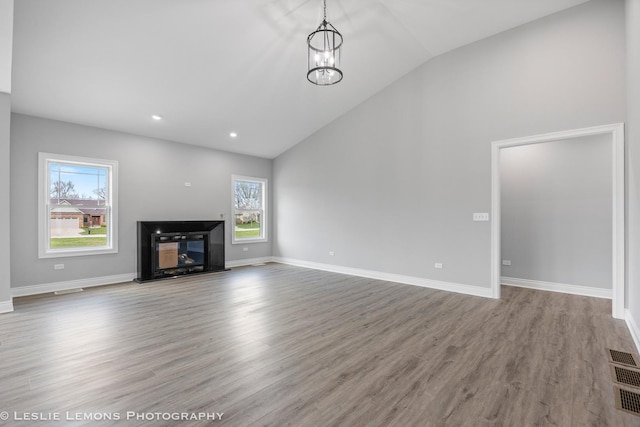 unfurnished living room with recessed lighting, lofted ceiling, a glass covered fireplace, baseboards, and wood finished floors